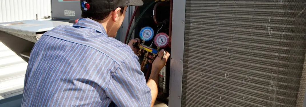HVAC technician servicing a condenser unit in Dedham